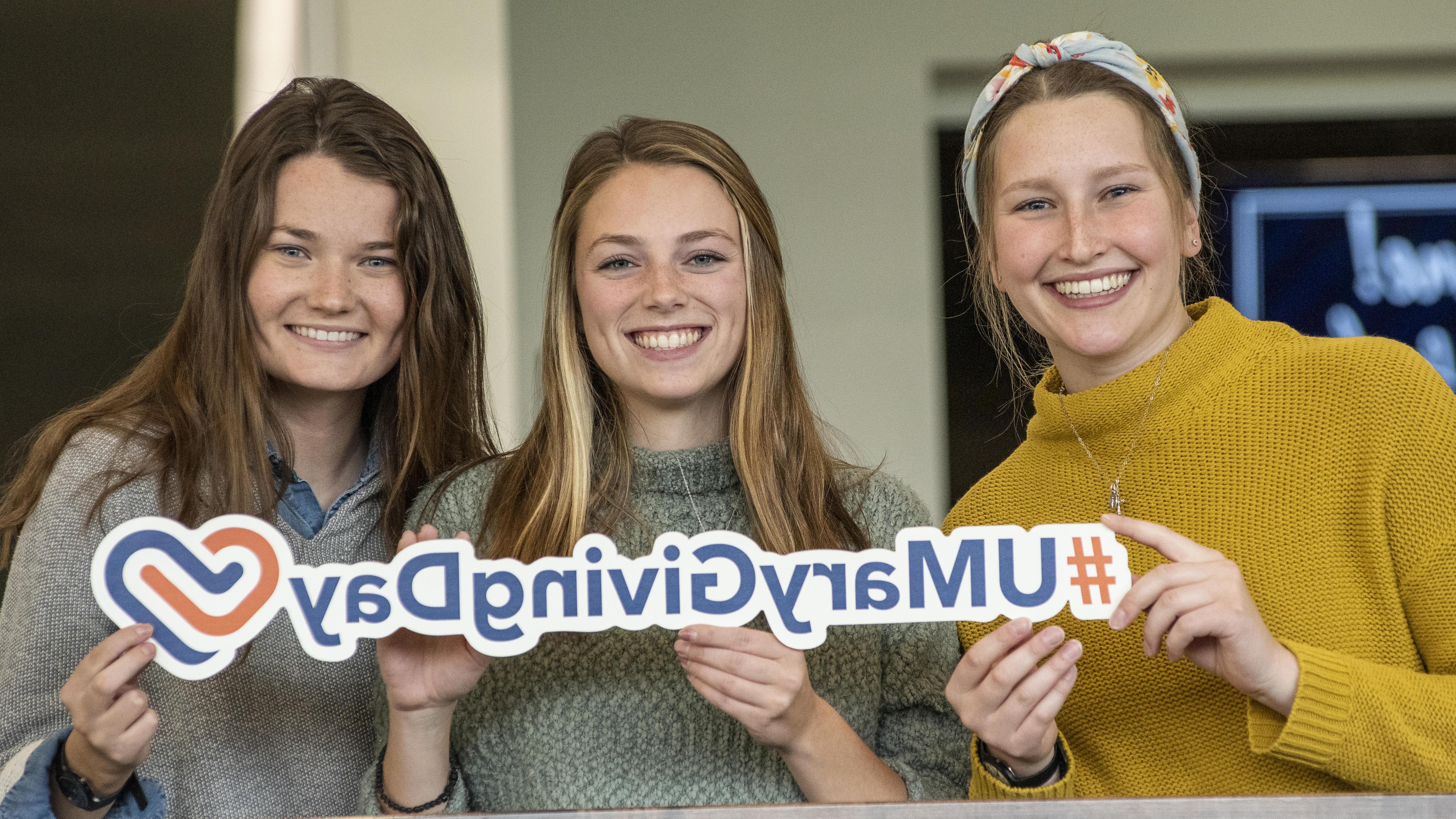 Three female students holding a #UMaryGivingDay sign